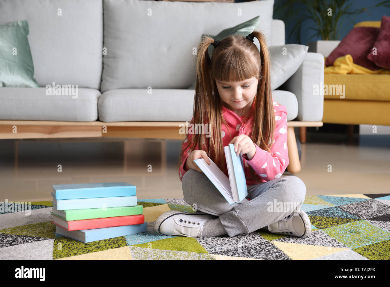 Cute little girl reading book at home Stock Photo - Alamy