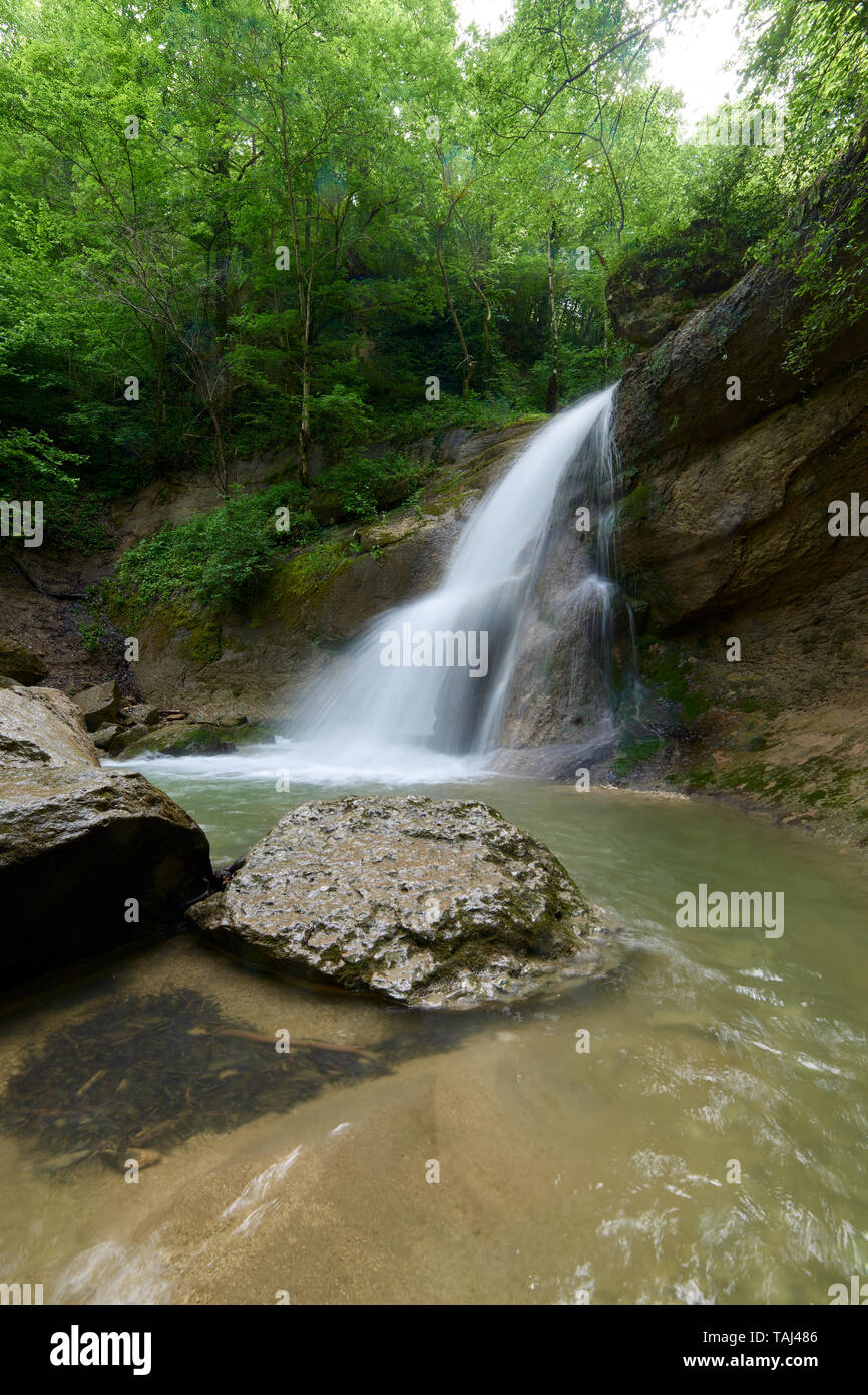Waterfall on a mountain river with green water and spring green forest ...