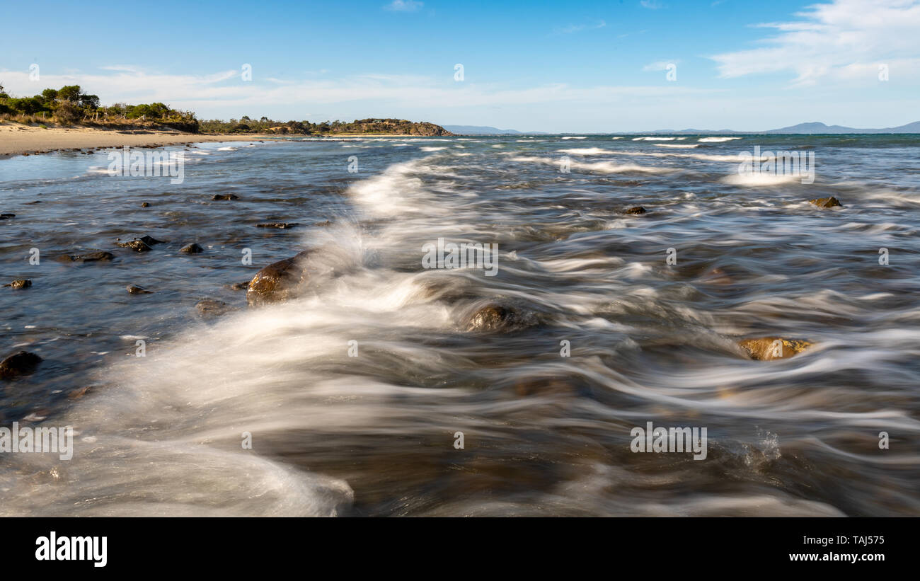 Wave Breaking Over Rocks, Motion Blur, Beach in Background Stock Photo