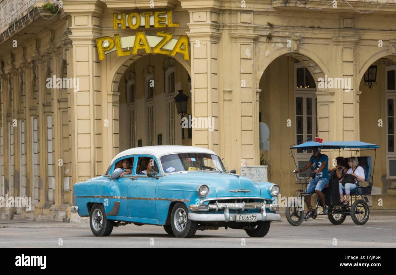 Havana, Cuba - A taxi and a bicycle taxi pass in front of Hotel Plaza near Parque Central. Classic American cars from the 1950s, imported before the U Stock Photo
