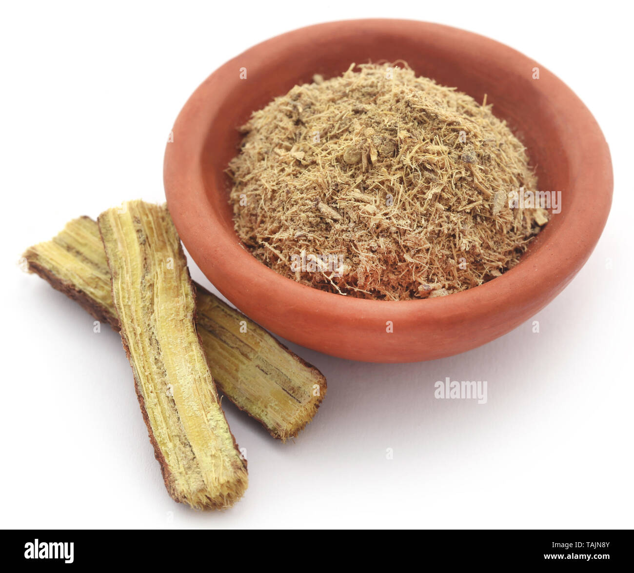 Liquorice stick and ground powder in a bowl over white background Stock Photo