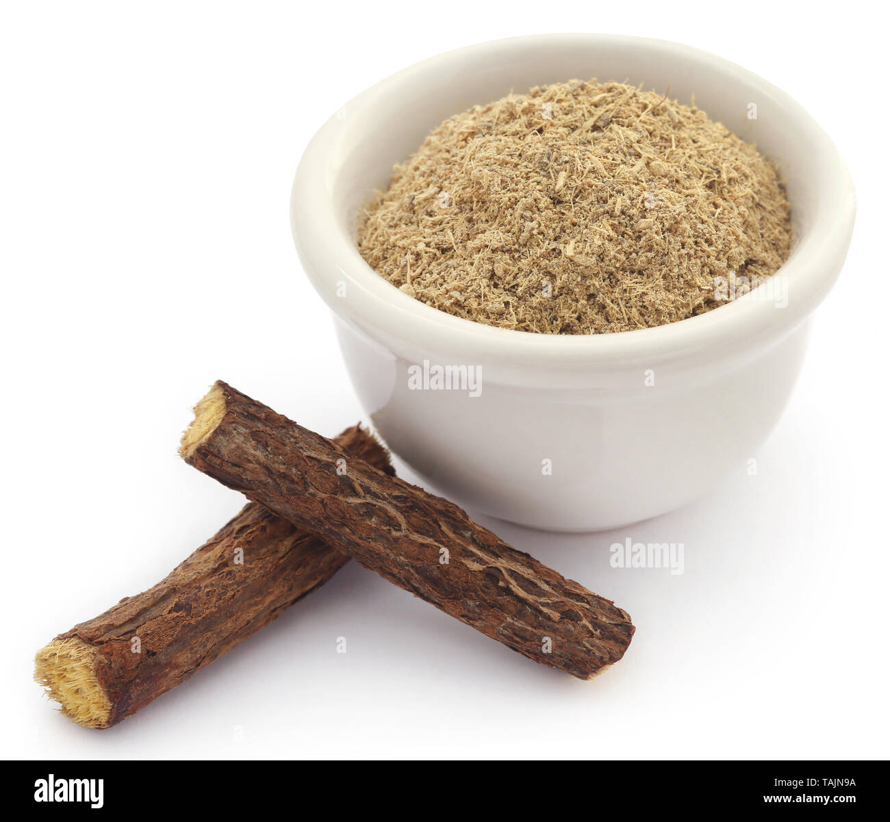 Liquorice stick and ground powder in a bowl over white background Stock Photo