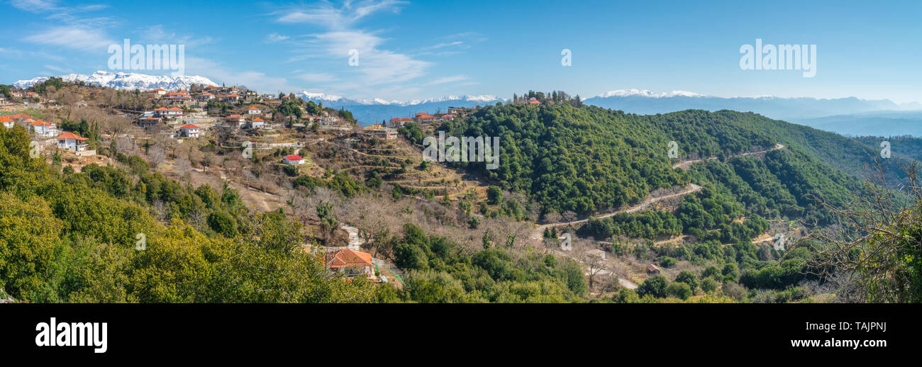 Panoramic view of small mountain town in the Greek countryside, with snowcapped mountains in the background. Rural Greek hamlet up in the hillside. Stock Photo