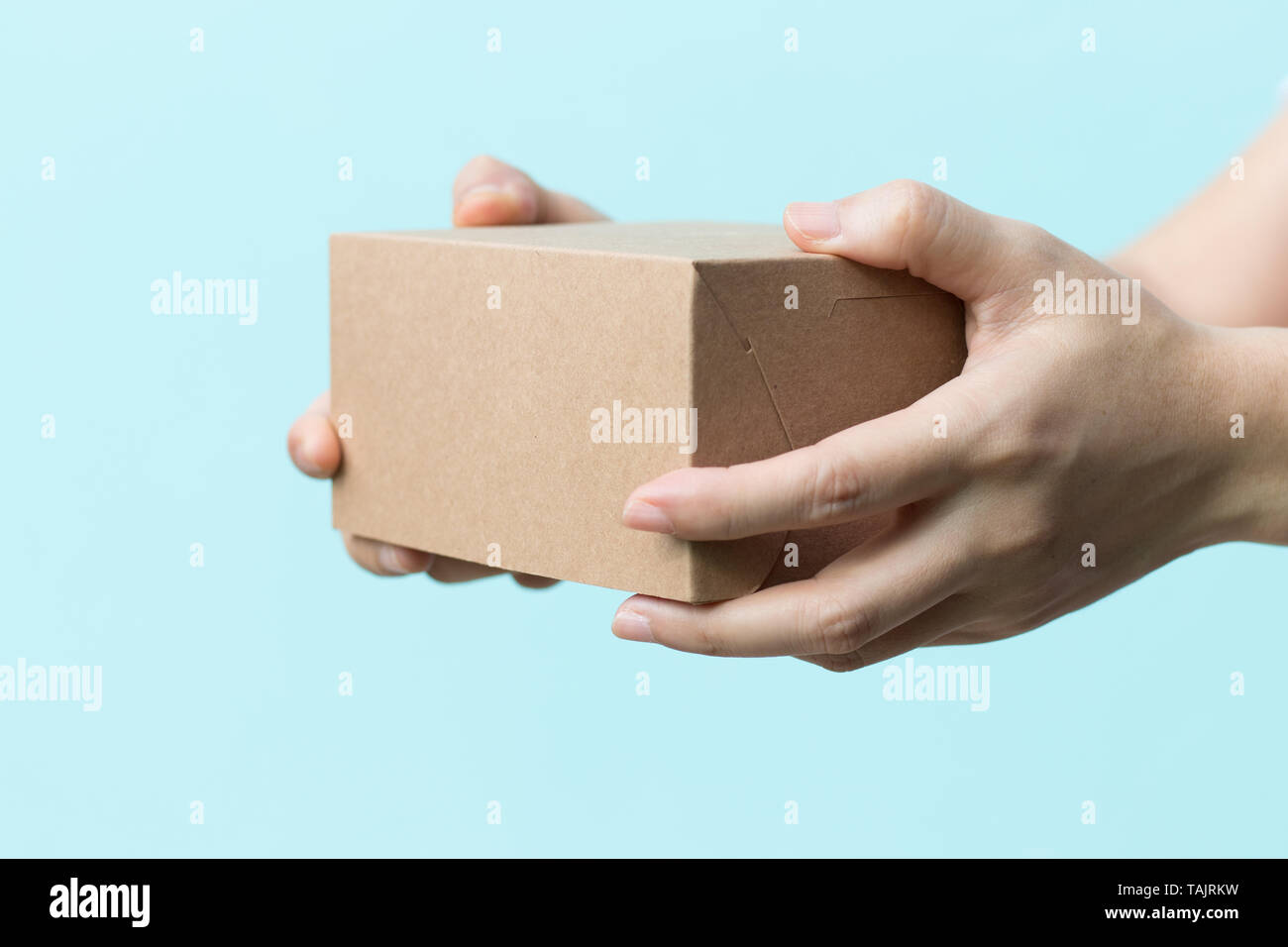 Woman hand hold the brown corrugated box on blue wall background with