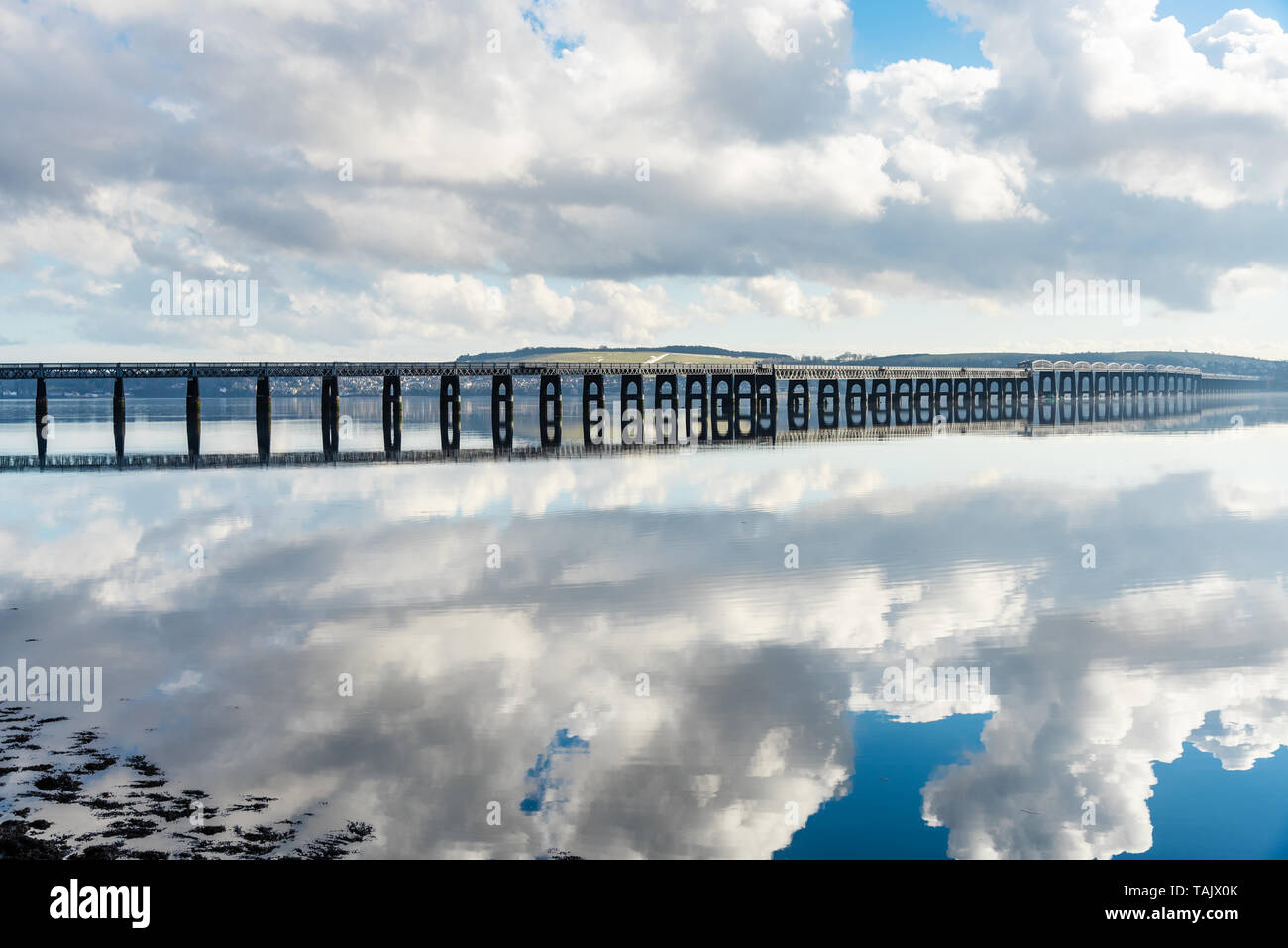 View of an empty railway bridge spannig a river on a partly cloudy winter morning. Reflection in water. Stock Photo