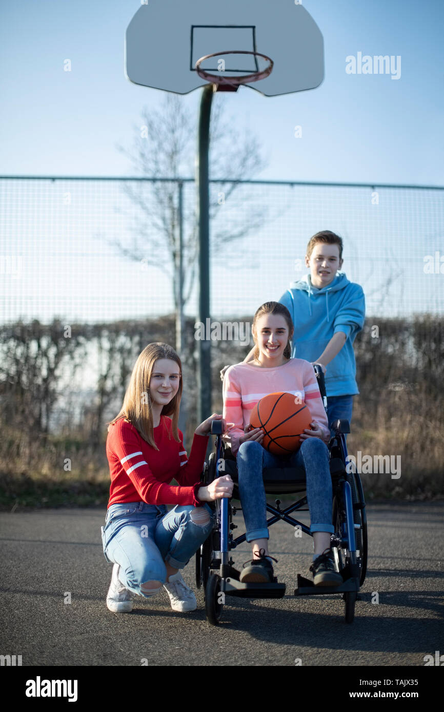 Portrait Of Teenage Girl In Wheelchair Playing Basketball With Friends Stock Photo