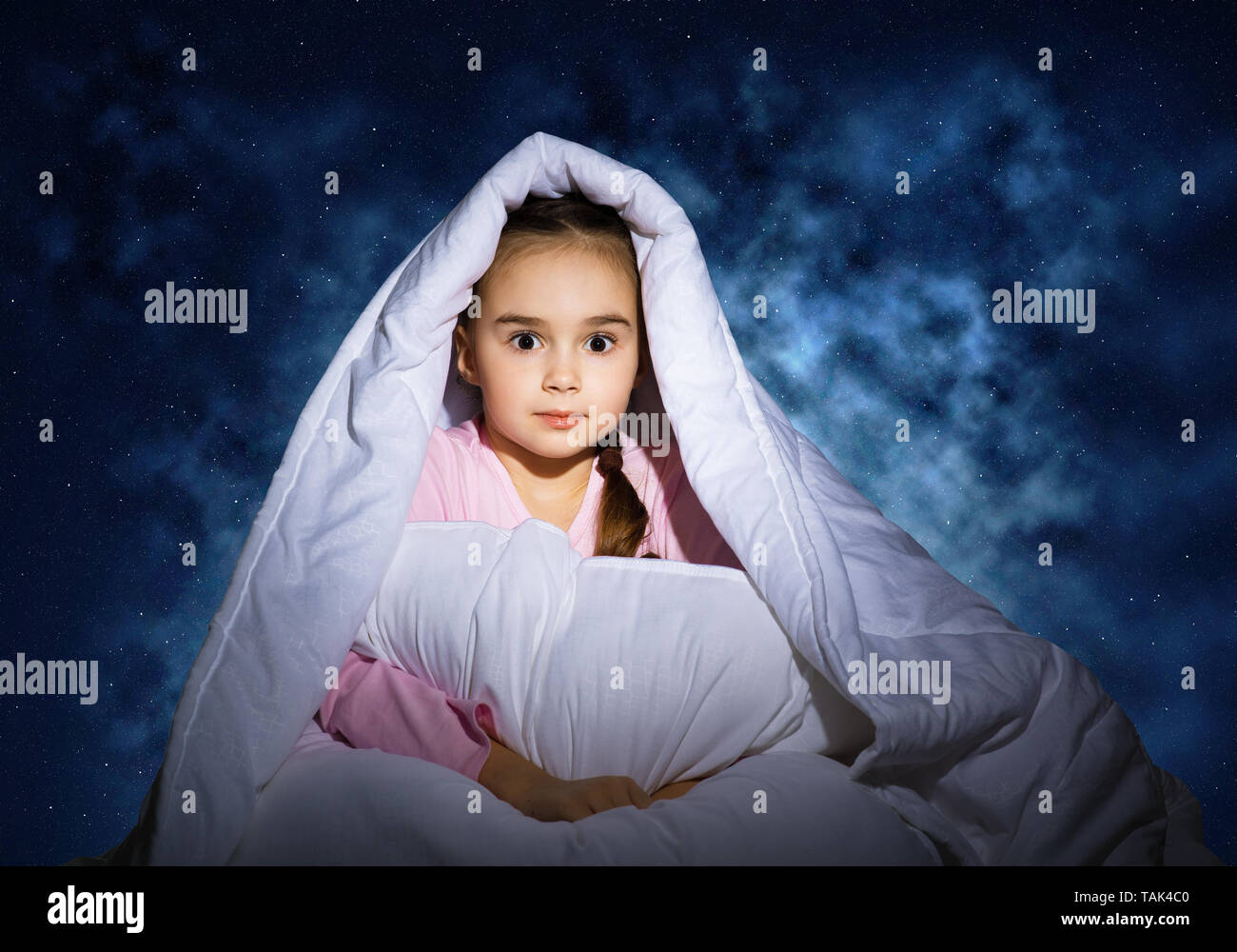 Scared girl with pillow hiding under blanket Stock Photo