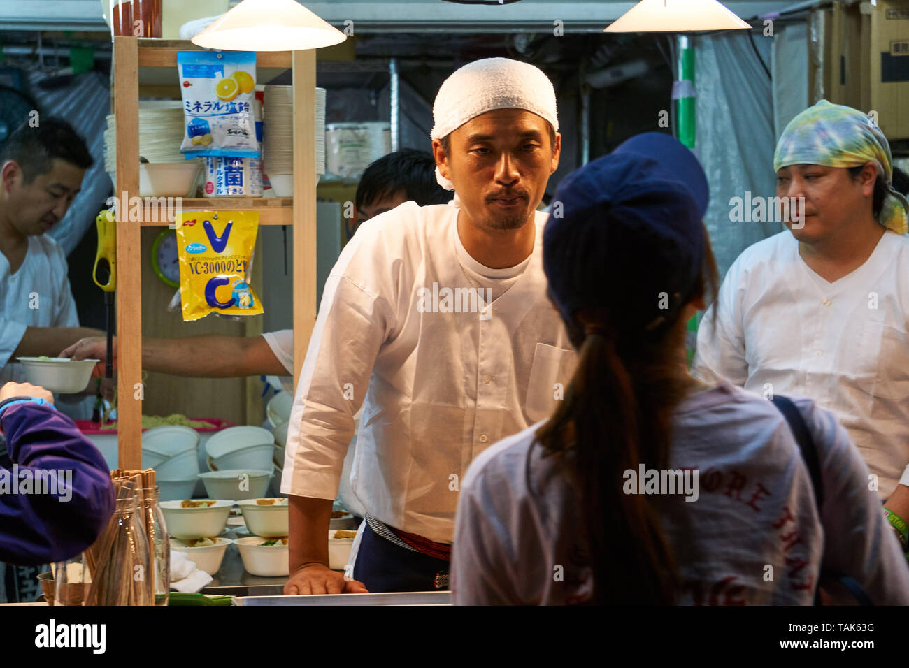 A Japanese woman makes an order at a food stall at the 2016 Fuji Rock Festival, while the Japanese chef waits impatiently. Stock Photo