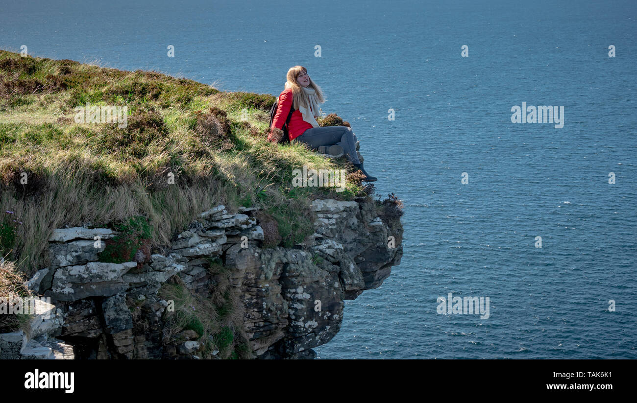 Young woman sitting on the edge of a cliff at the Irish west coast ...