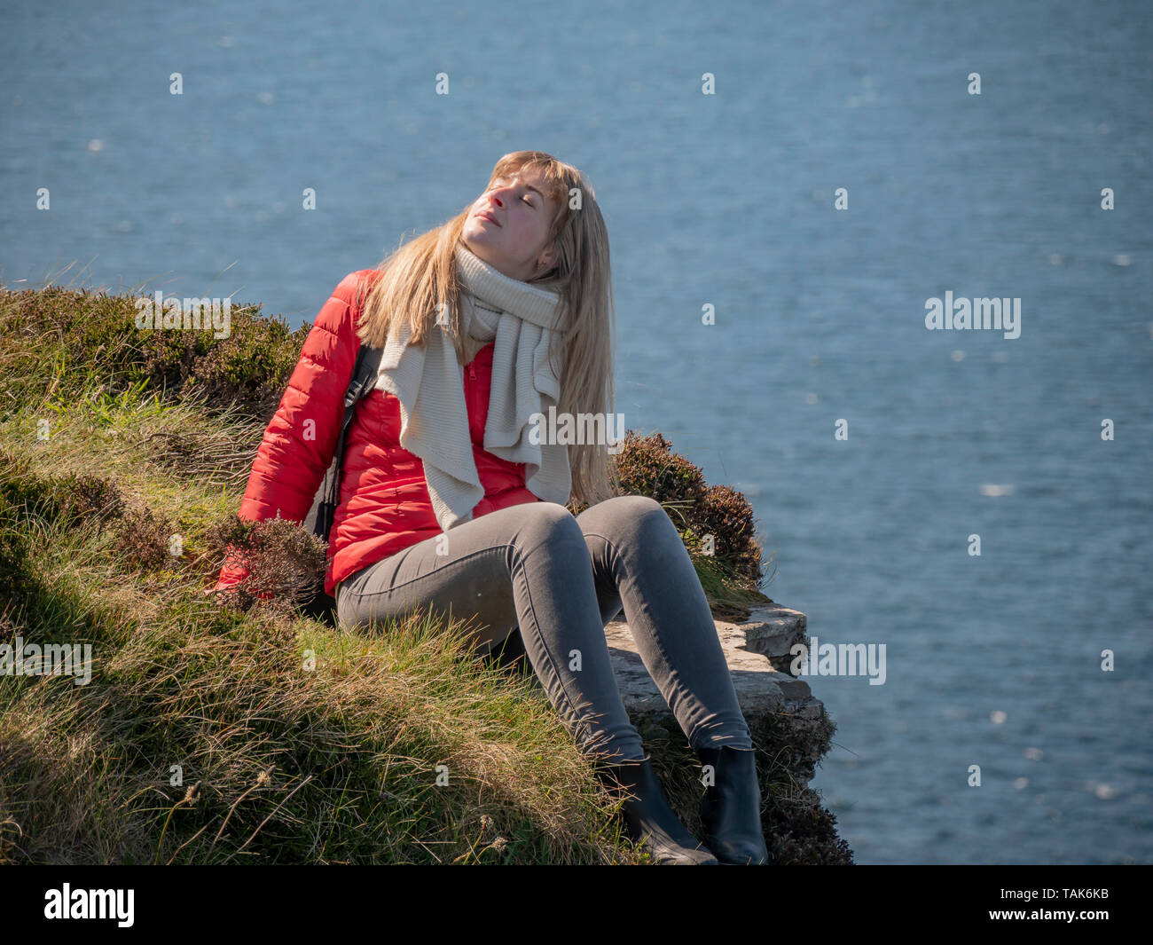 Young woman sitting on the edge of a cliff at the Irish west coast ...