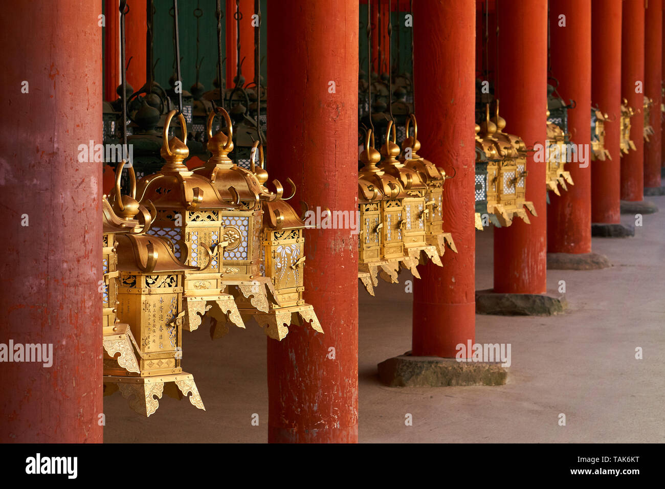 Traditional gold colored metal Japanese lanterns hang between wooden vermilion columns at Kasuga Taisha Grand Shrine in Nara, Japan. Stock Photo