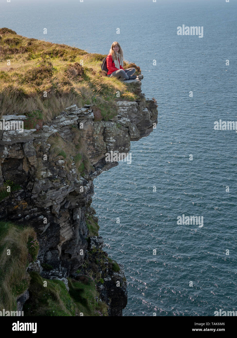 Young woman sitting on the edge of a cliff at the Irish west coast ...