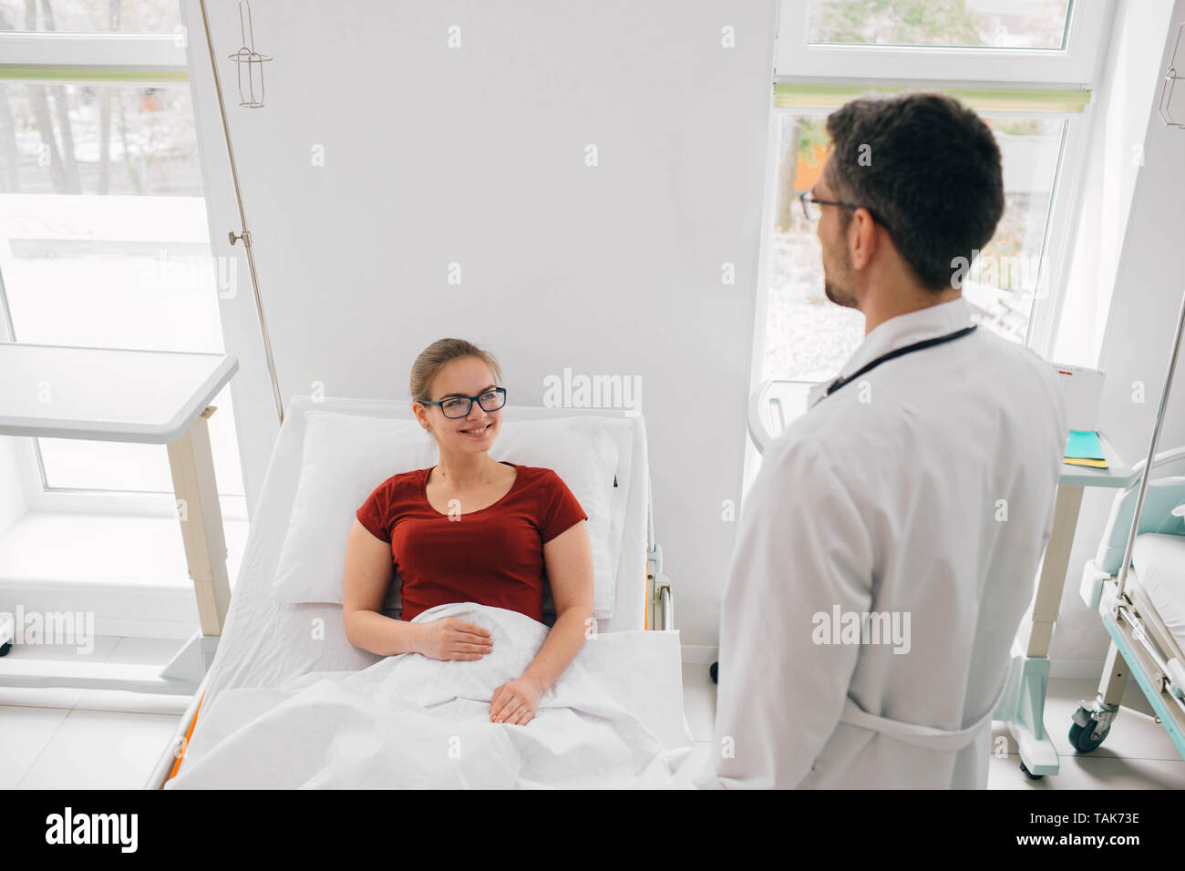 Woman lying in a hospital ward and positively looking to her doctor. Feeling better after treatment Stock Photo