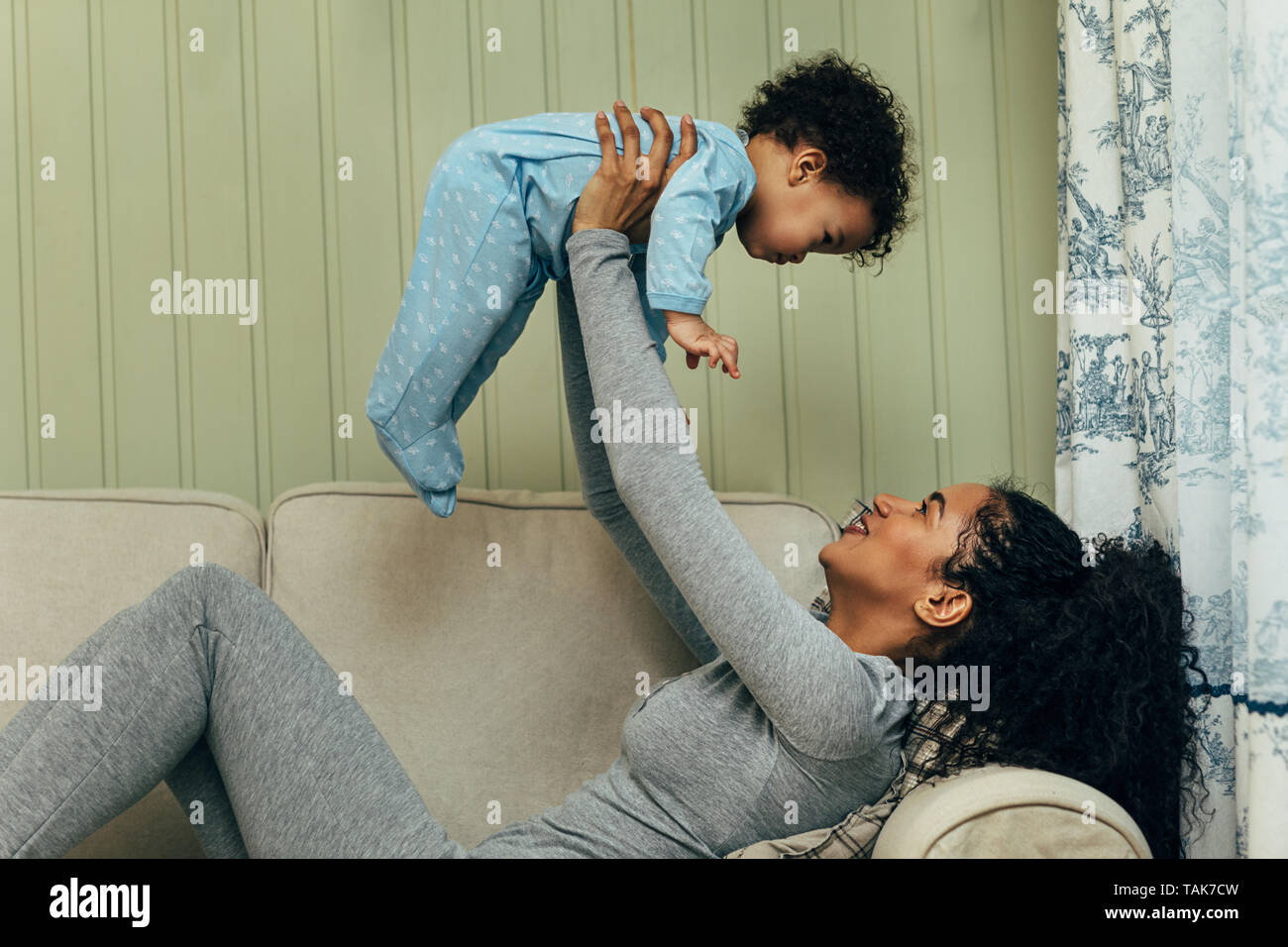 Young mother sitting on a sofa and lifting her baby in living room