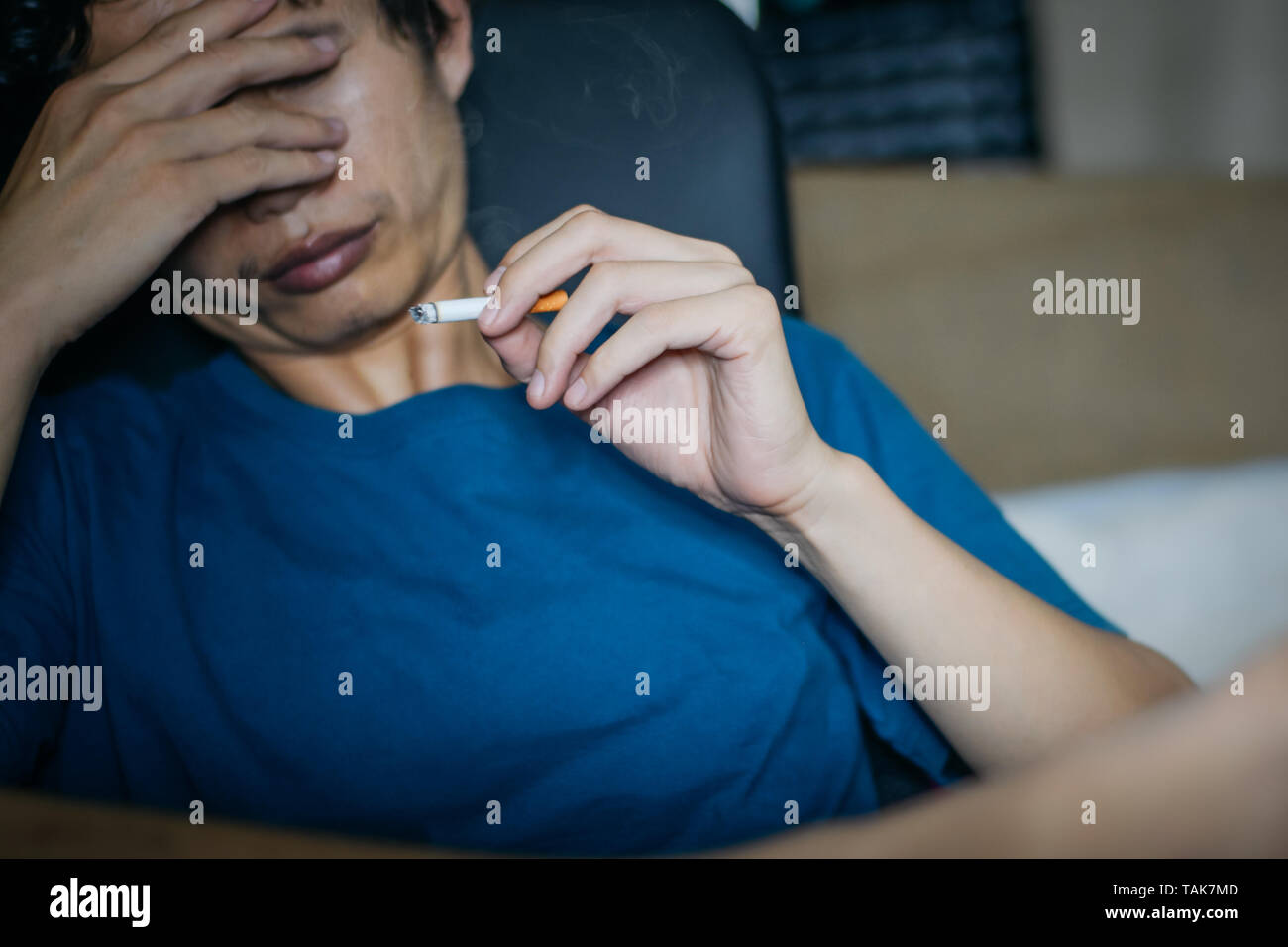 Man smokes a cigarette on work chair at working room in home office when his eliminate stress from work hard at night time Stock Photo