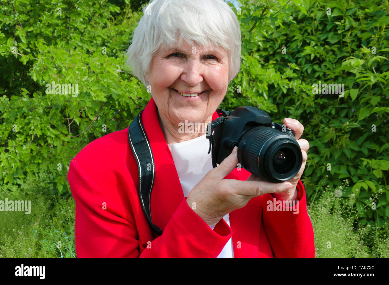 portrait of smile, happy grandmother enjoy her hobby at sun day. modern caucasian granny is professional photographer . photocamera in adult hand of old lady. pensioner use technology Stock Photo