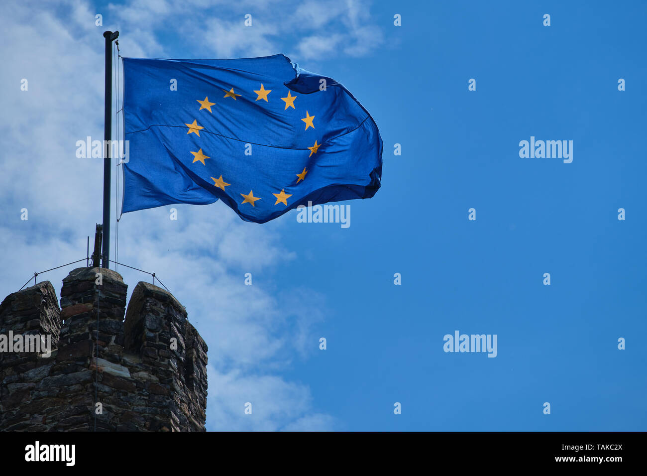 photography of a waving flag of Europe on a tower against blue sky with clouds Stock Photo