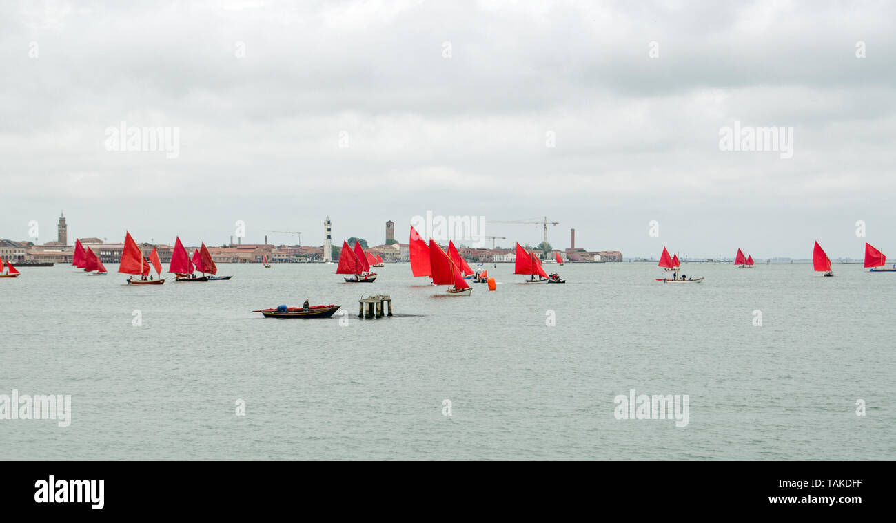 A regatta of Venetian sailing boats, all sporting red painted sails, on the lagoon near Murano.  Part of the Red Regatta event organised by artist Mel Stock Photo