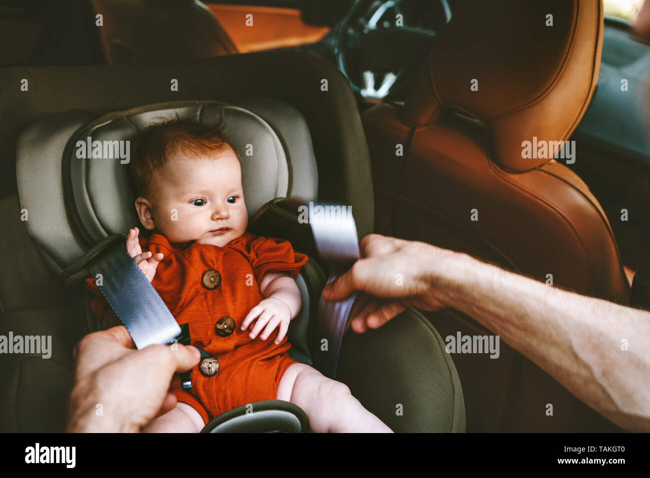 Infant baby in safety car seat and father fastens belt family road trip lifestyle vacations with child security transportation Stock Photo