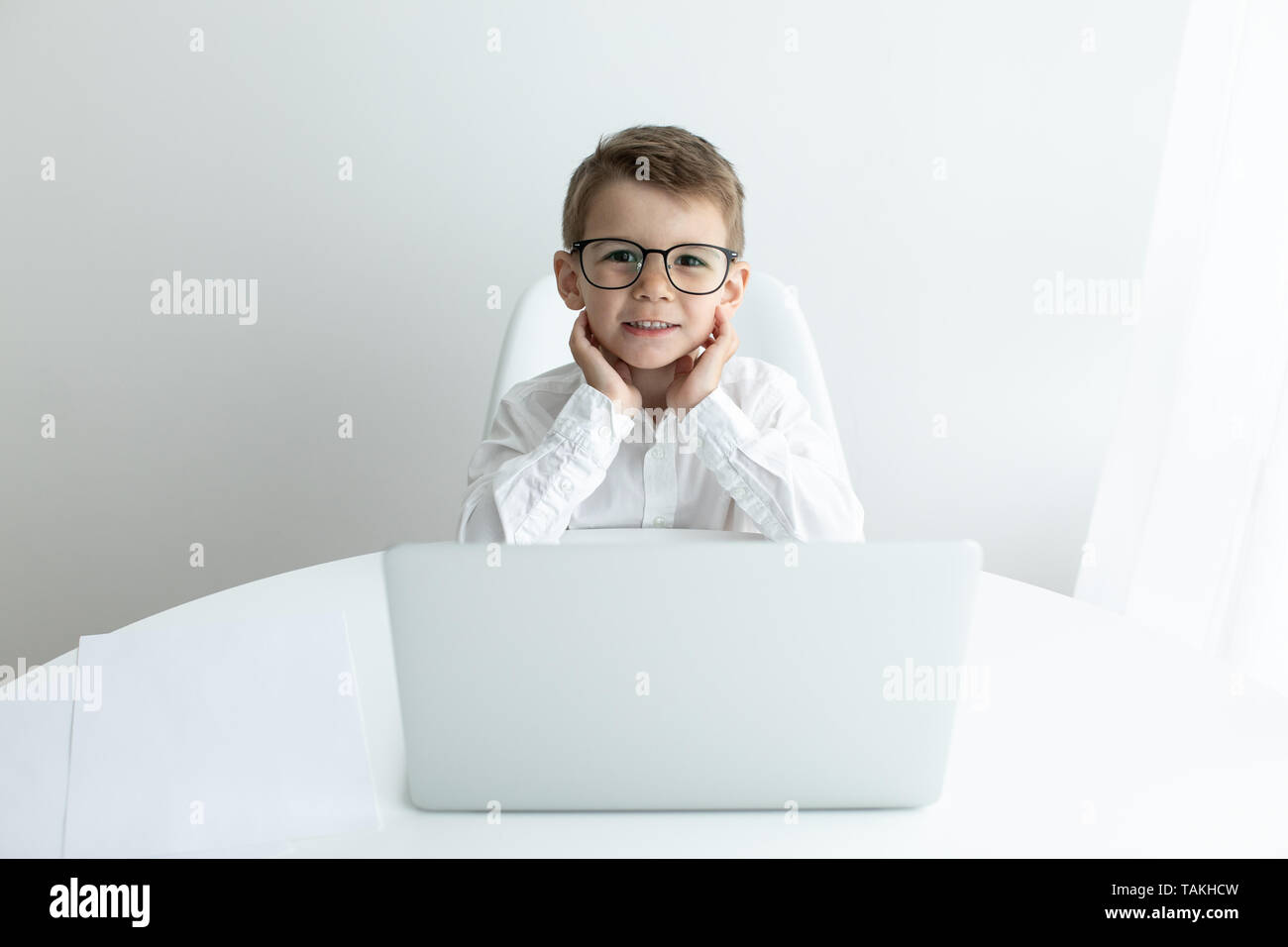 Cute little boy using laptop while doing homework against white ...
