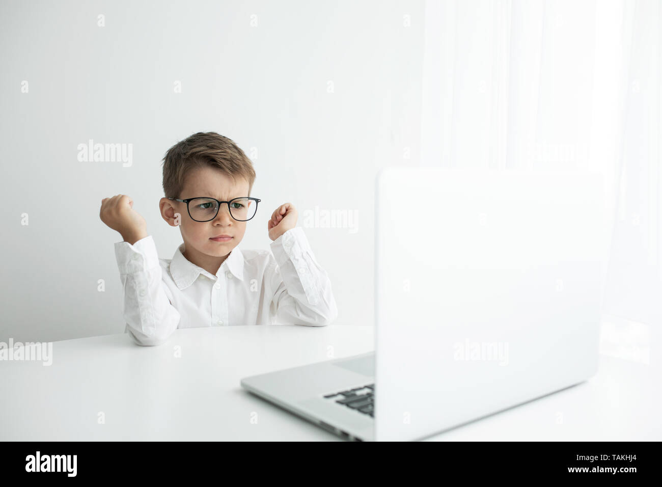 Cute little boy using laptop while doing homework in white room Stock ...