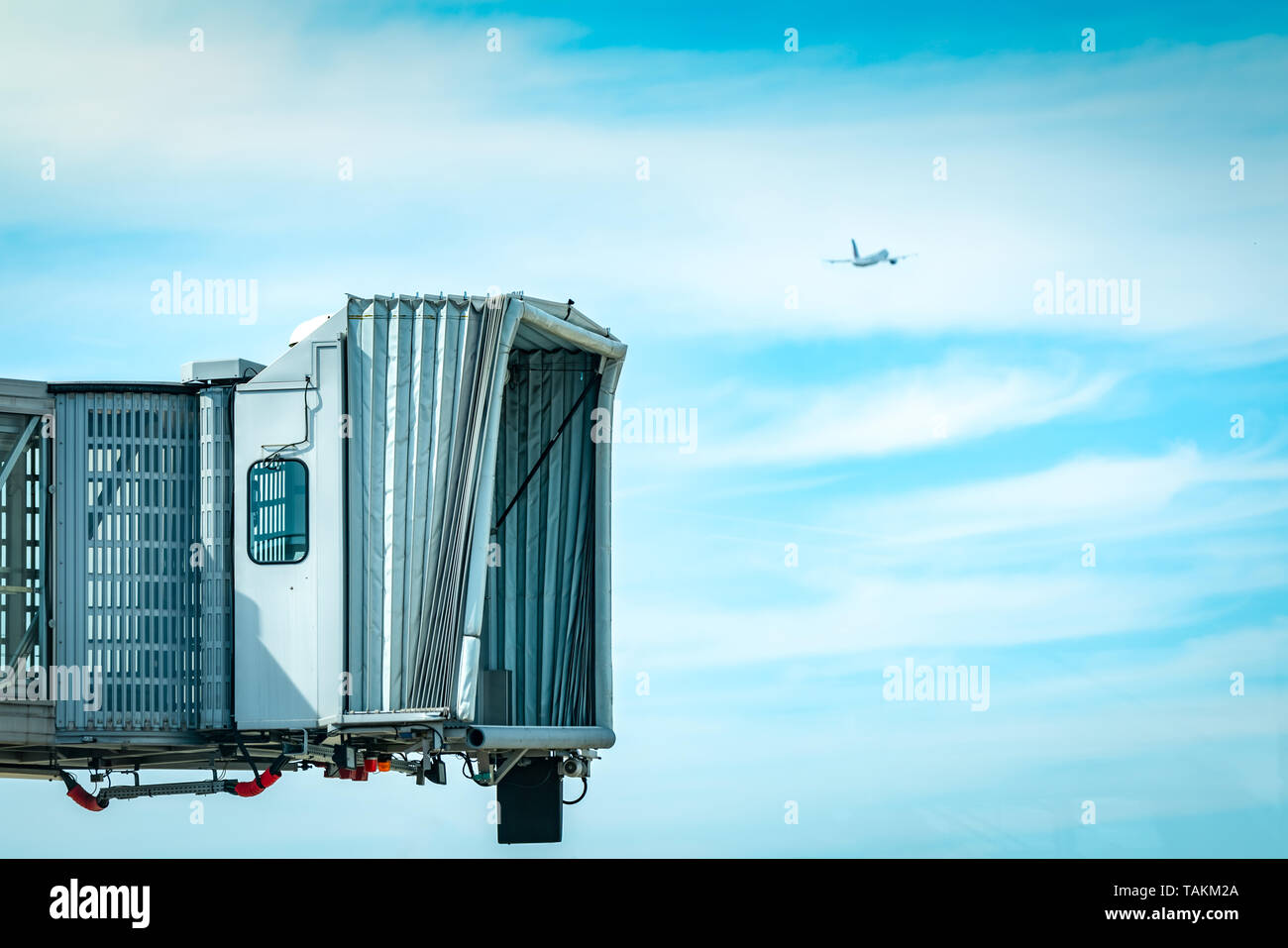 Jet bridge after commercial airline take off at the airport and the plane flying in the blue sky and white clouds. Aircraft passenger boarding bridge  Stock Photo