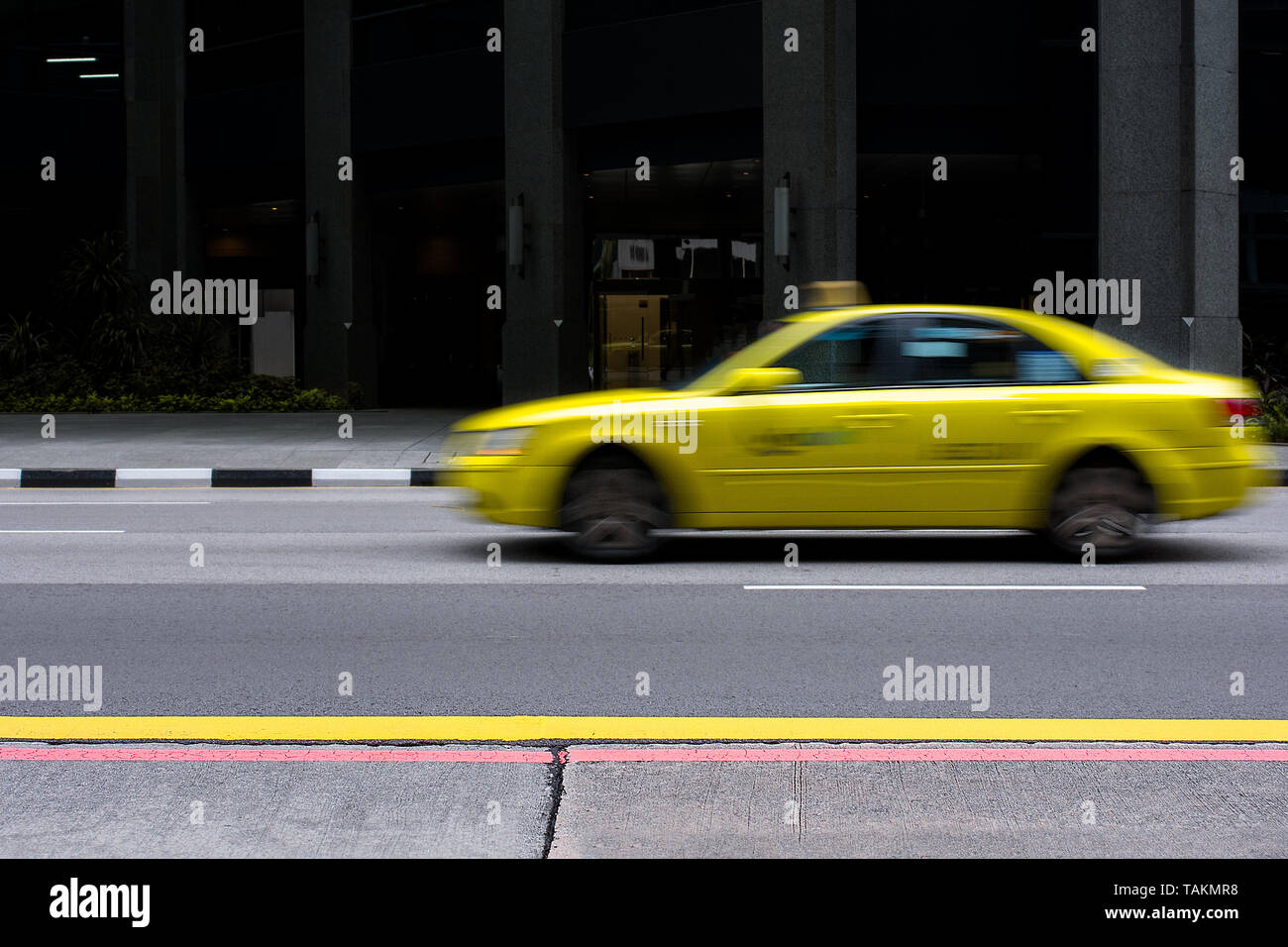Yellow taxi of Singapore drives past in a motion blur on empty city road. Stock Photo