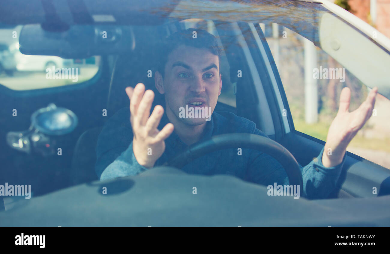 Angry man driving a vehicle arguing and gesturing shaking his hands perplexed. Irritated and furious driver guy negative facial expression, seated in  Stock Photo