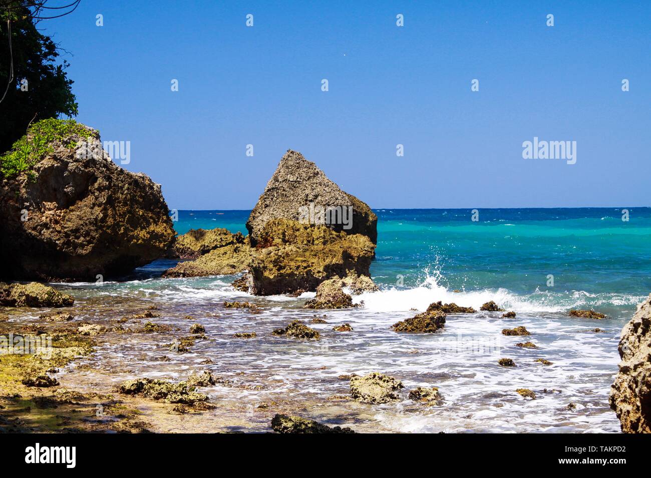 View beyond sharp rocks on turquoise rough sea with wave breakers and ...