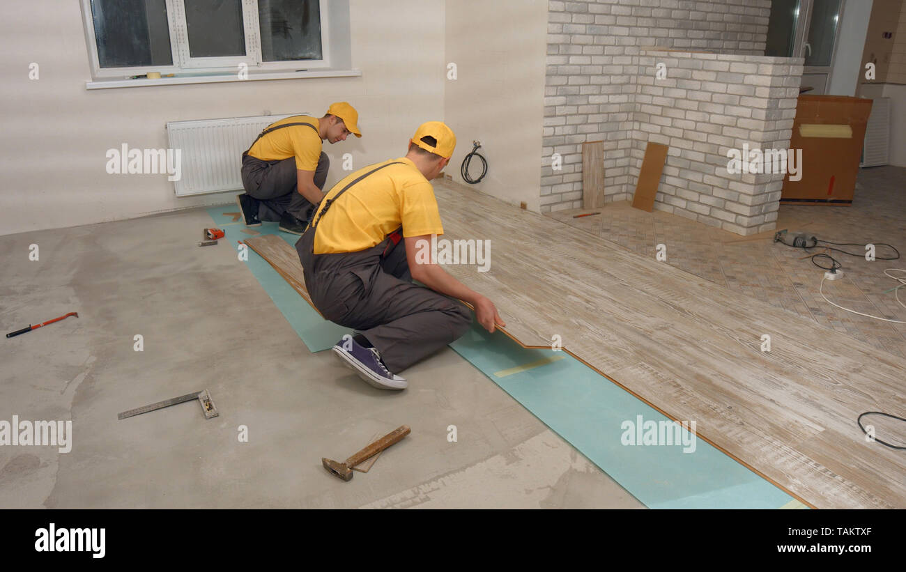Team of builders make renovation of apartment. Construction workers laying floor board Stock