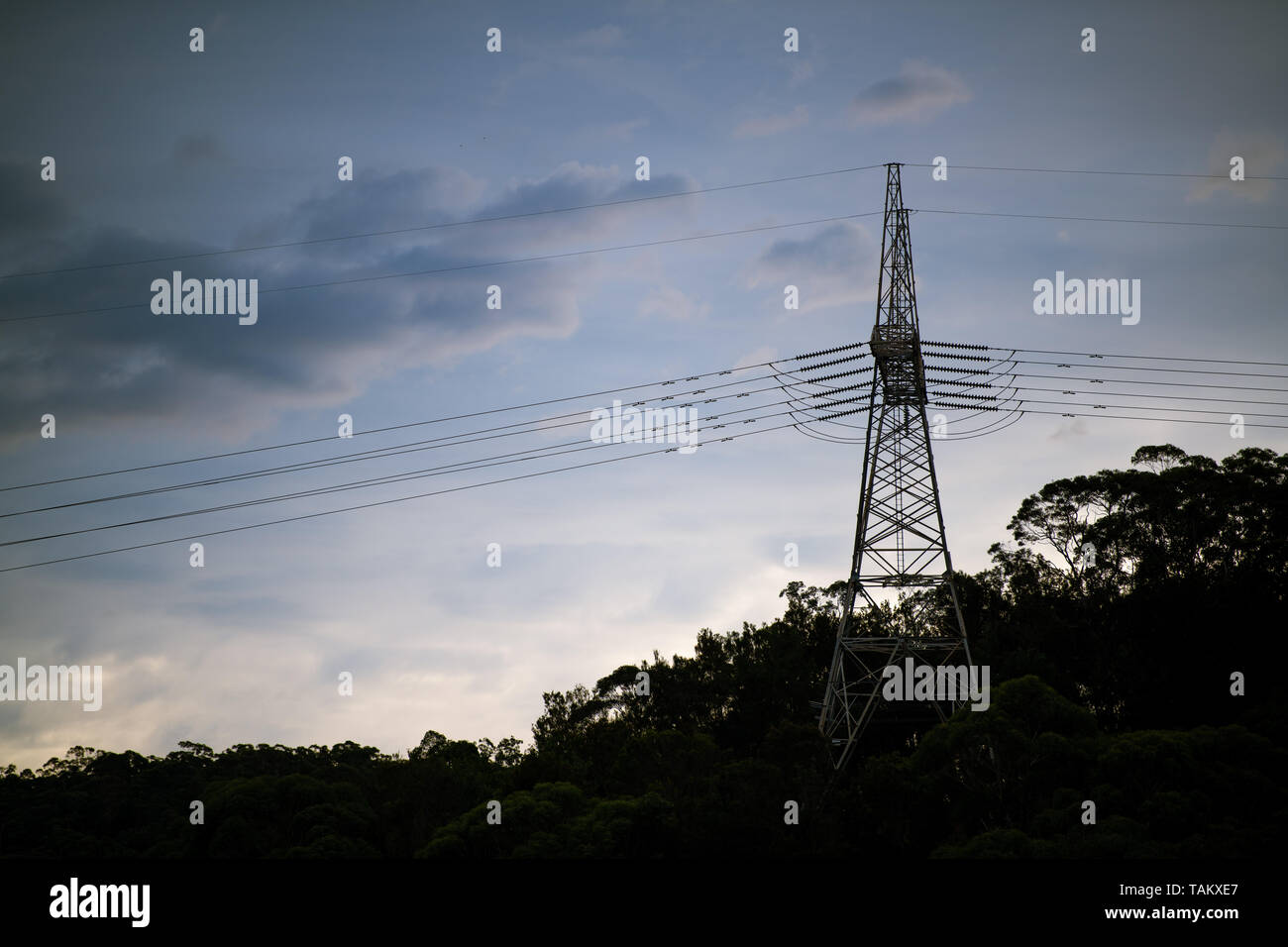 High Voltage power lines and tower silhouetted against cloudy sky in ...