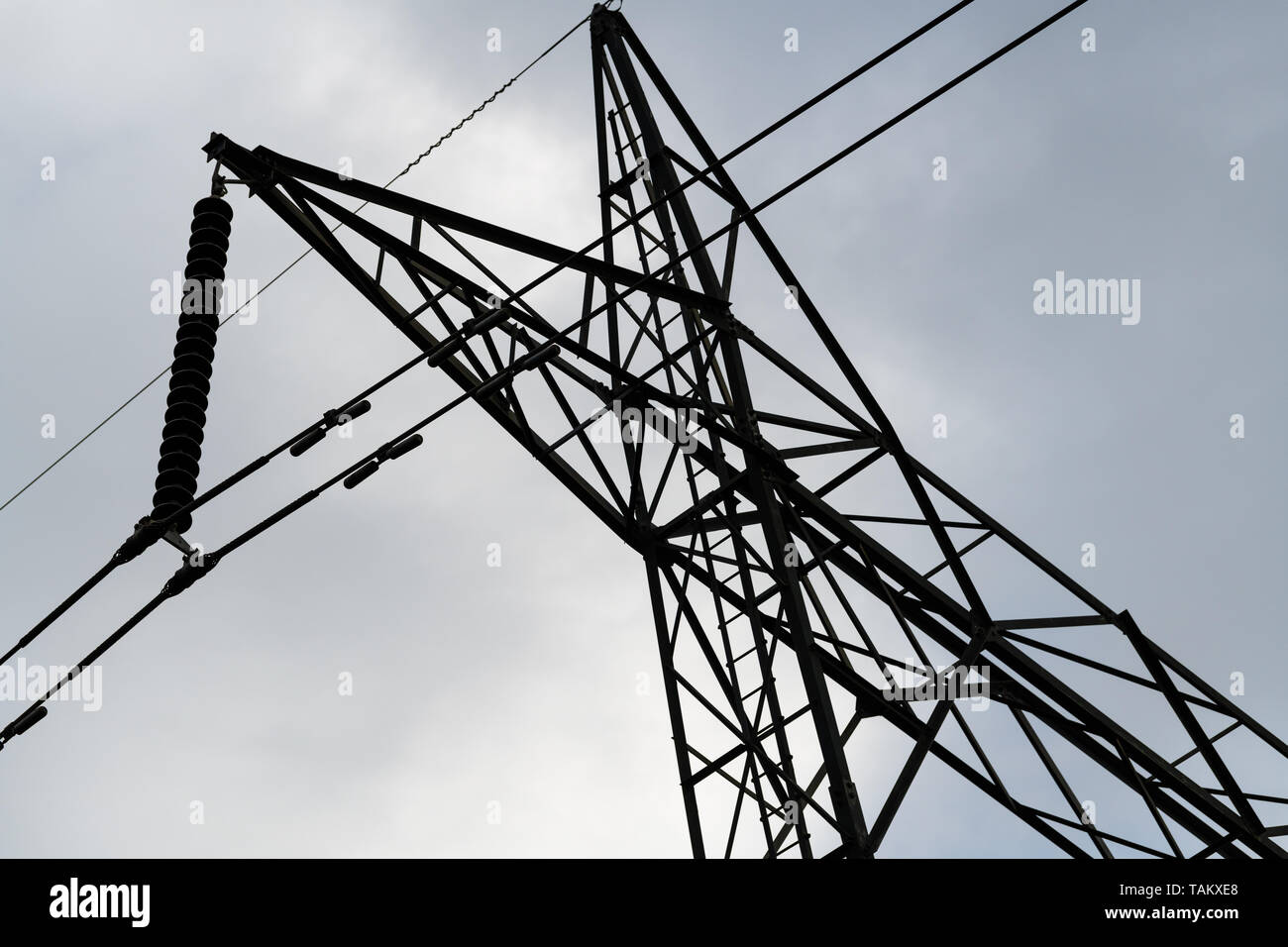 High Voltage power lines and tower shot from beneath under a cloudy sky ...