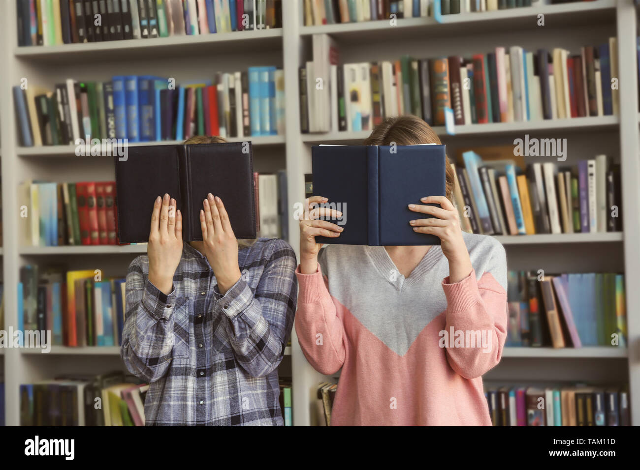 Young women hiding faces behind books in library Stock Photo