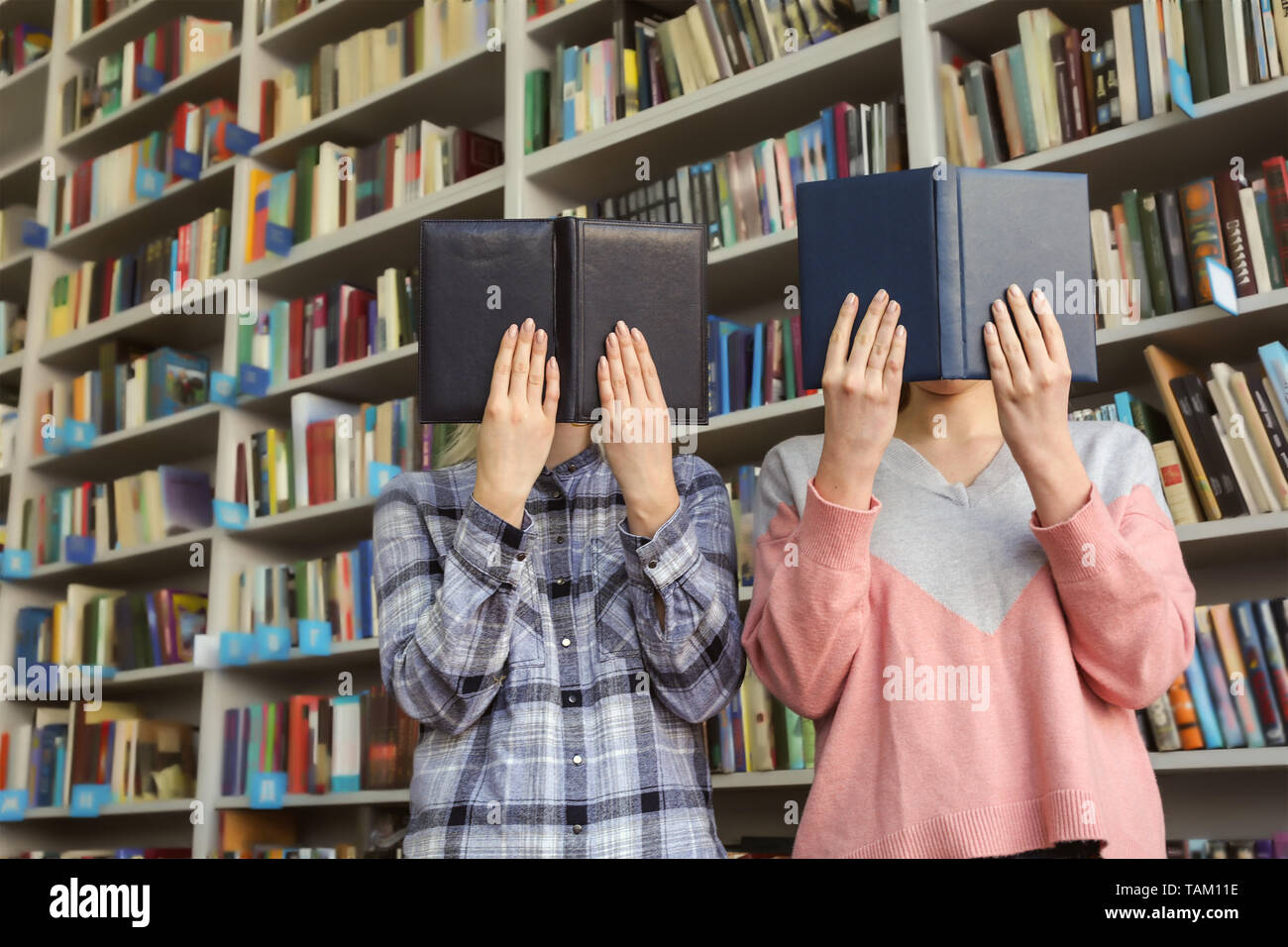 Young women hiding faces behind books in library Stock Photo
