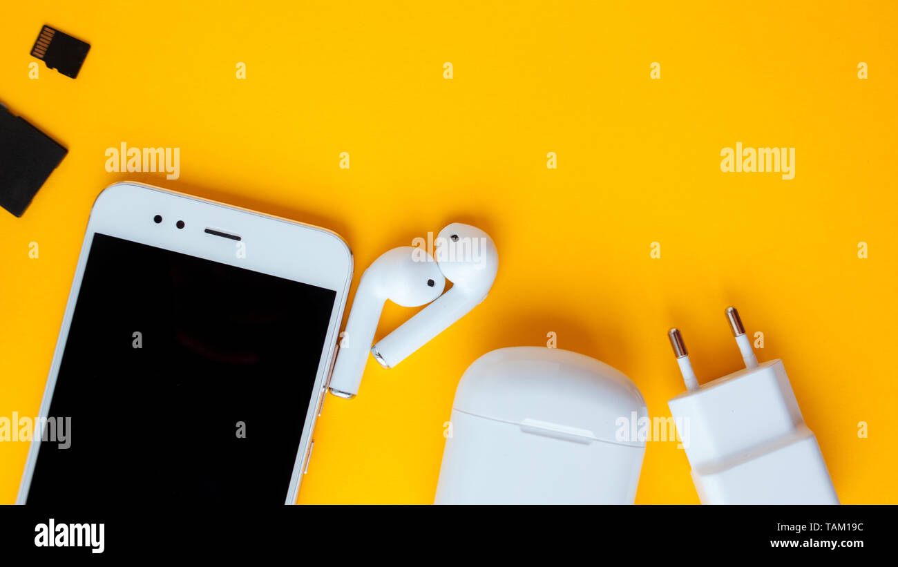 Smartphone and wireless headphones. Charging and wire included. Mobile phone  and accessories on yellow background Stock Photo - Alamy
