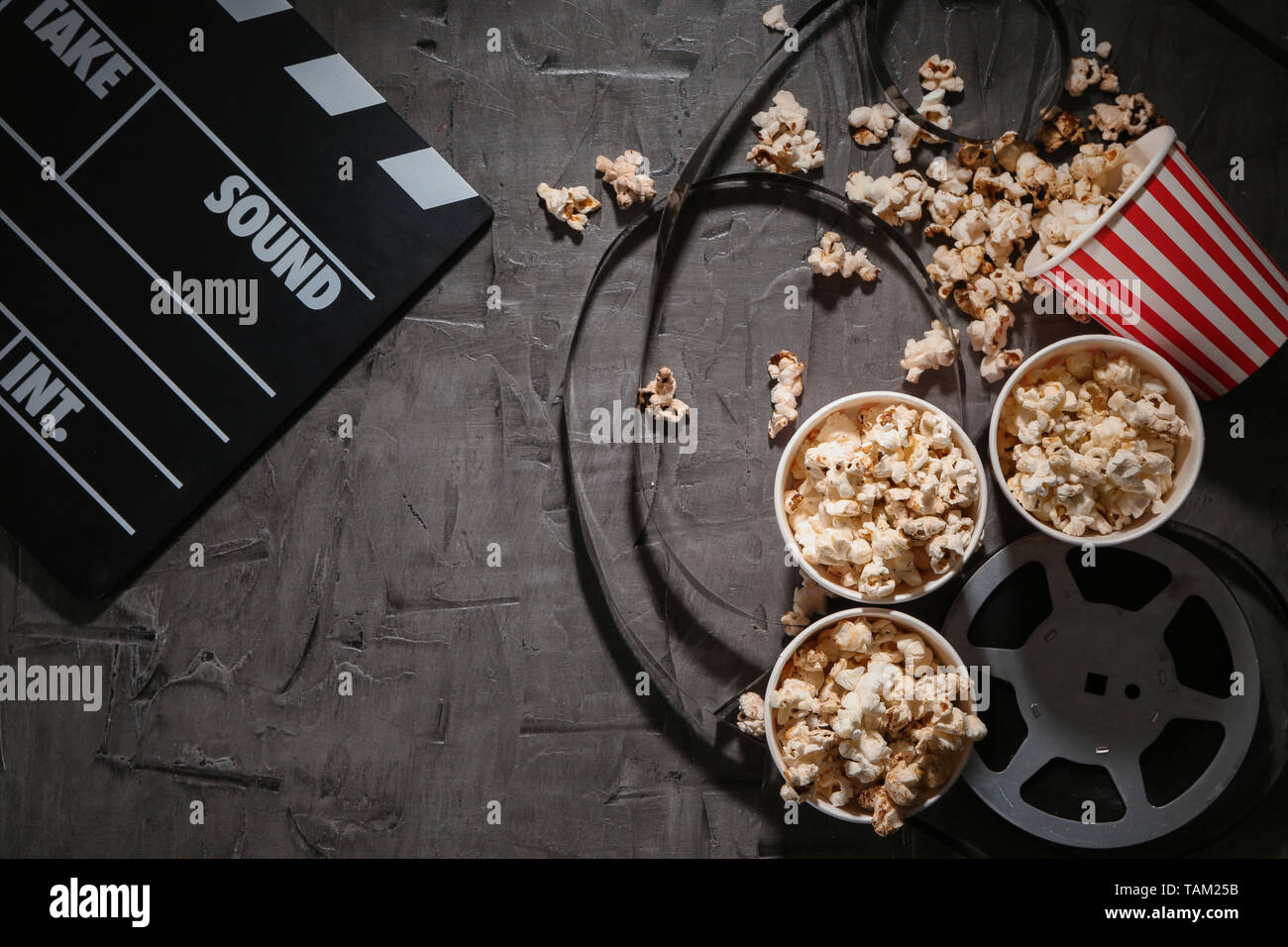 Composition with popcorn, cinema clapperboard and film on dark background Stock Photo