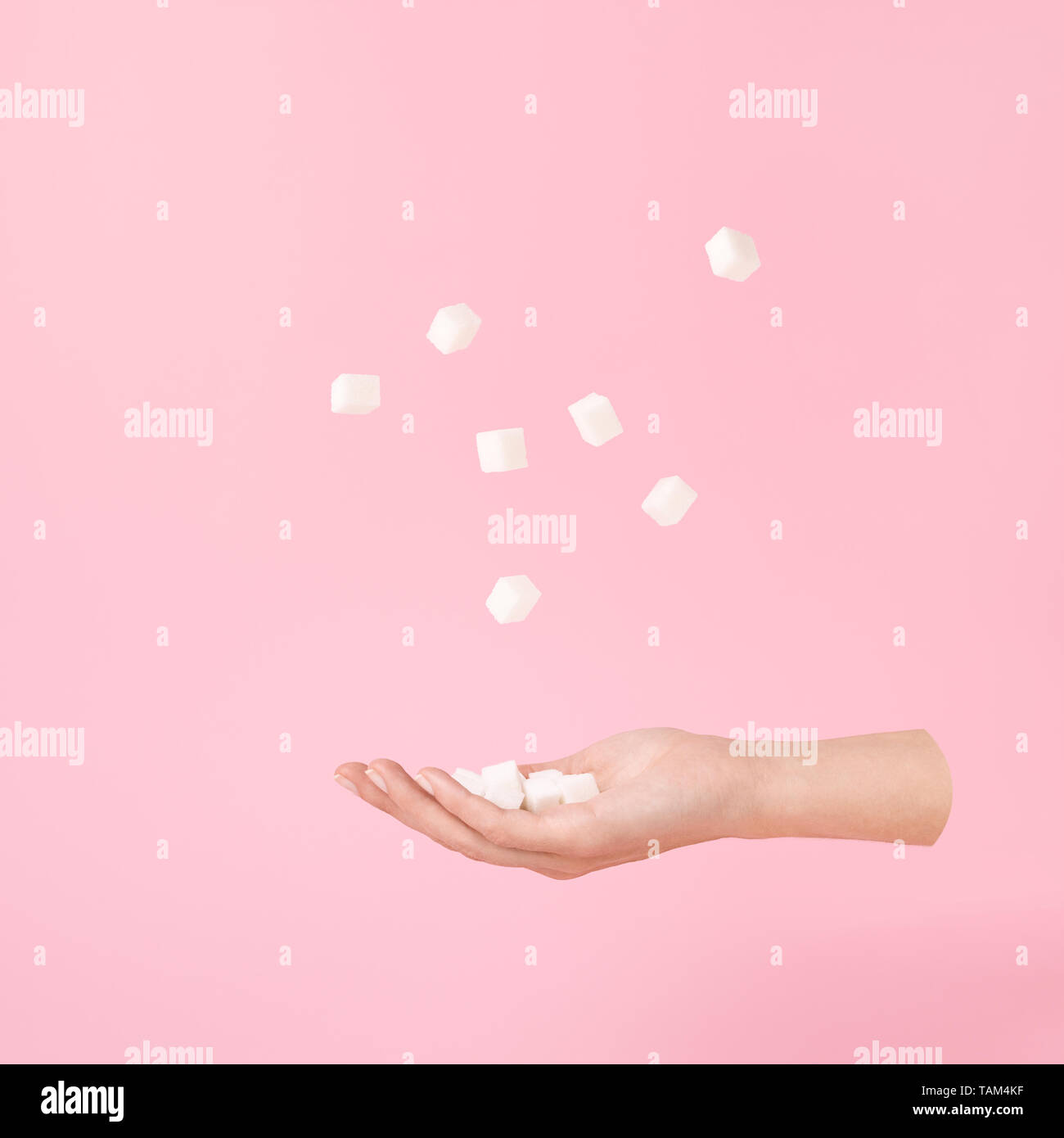 Flying female hand and sugar cubes levitation on pastel pink. Minimal or surrealism style. Sweet life concept. Stock Photo