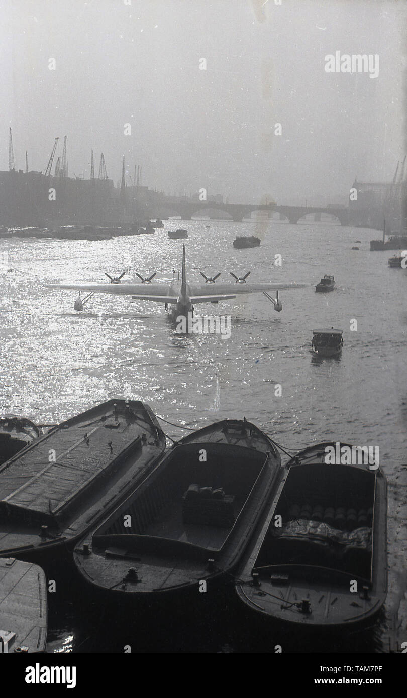 1960s, historical, a propellered seaplane, a flying boat, sitting down river by the docks and barges on the river Thames, London, England, UK. Stock Photo