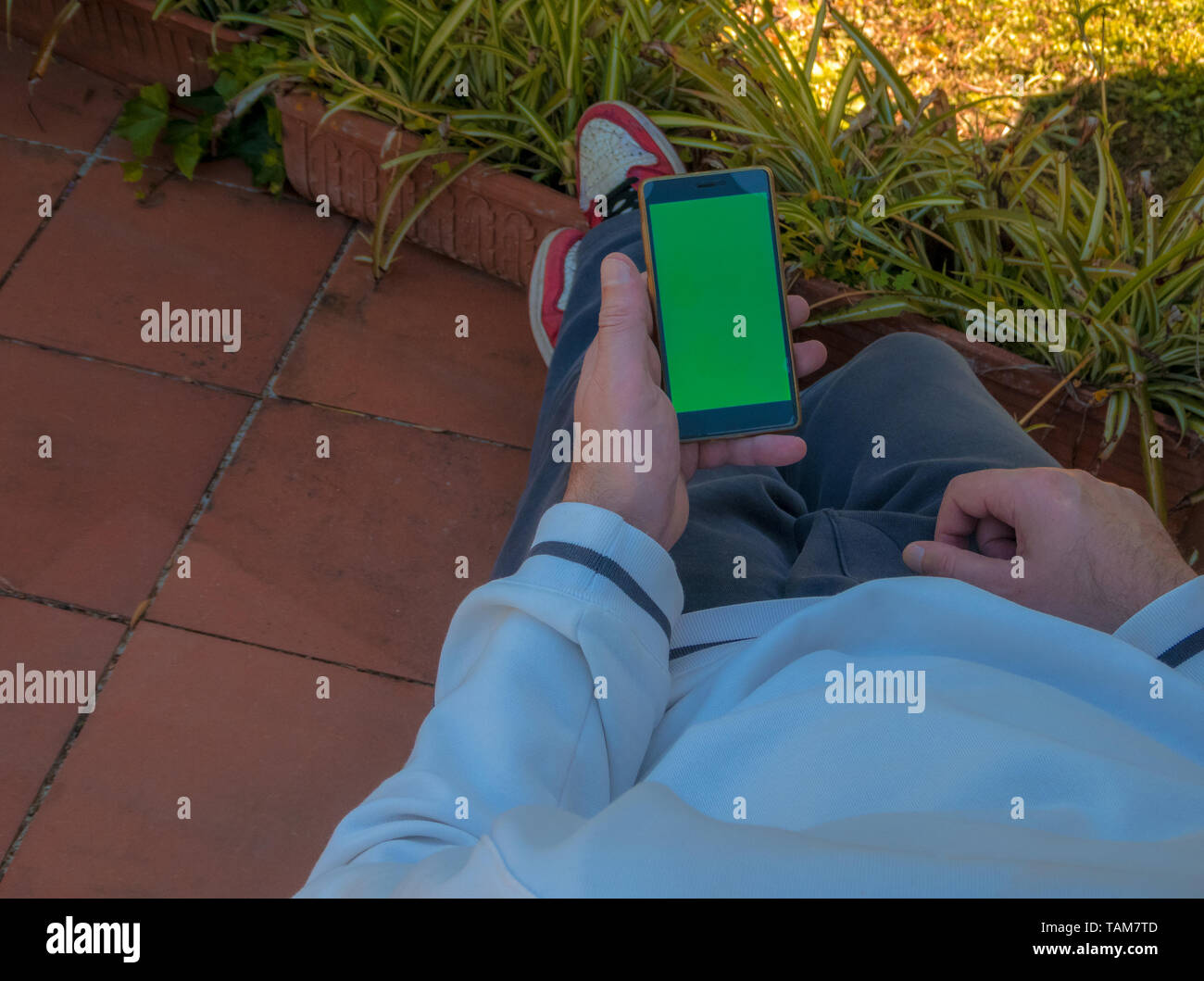 Man in a terrace room using Smartphone with Green Mockup Screen, Over