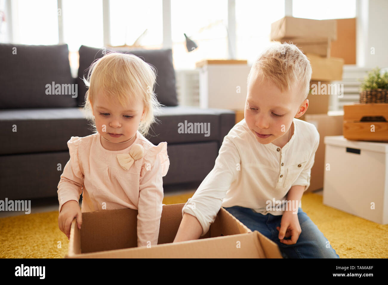 Serious curious brother and sister sitting on floor into new home and fining things while unpacking box together Stock Photo