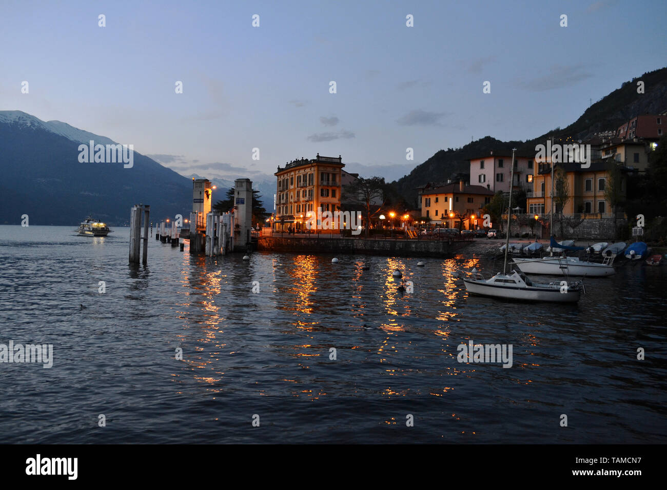 Varenna/Italy- April 6, 2014: Beautiful panoramic view to the lake Como with a passenger ship moving away from the Varenna port at sunset in spring. Stock Photo