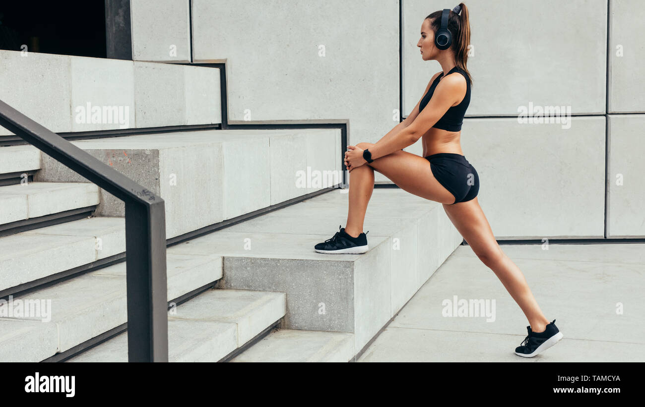 Side view of fitness woman stretching in morning. Sporty woman exercising outdoors on steps. Stock Photo