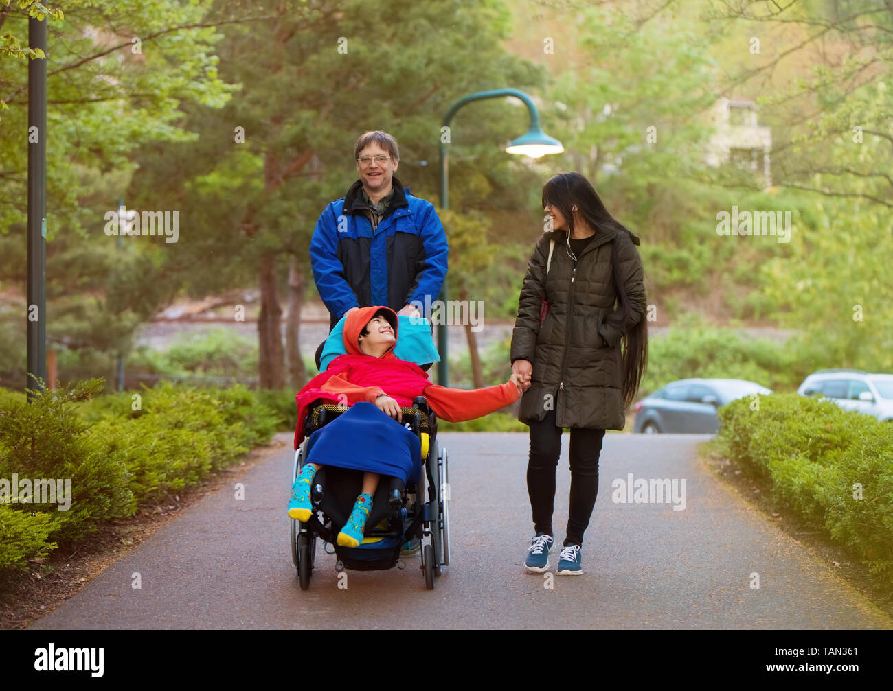 Disabled twelve year old biracial boy in wheelchair walking with father and older sister at park in cold weather Stock Photo