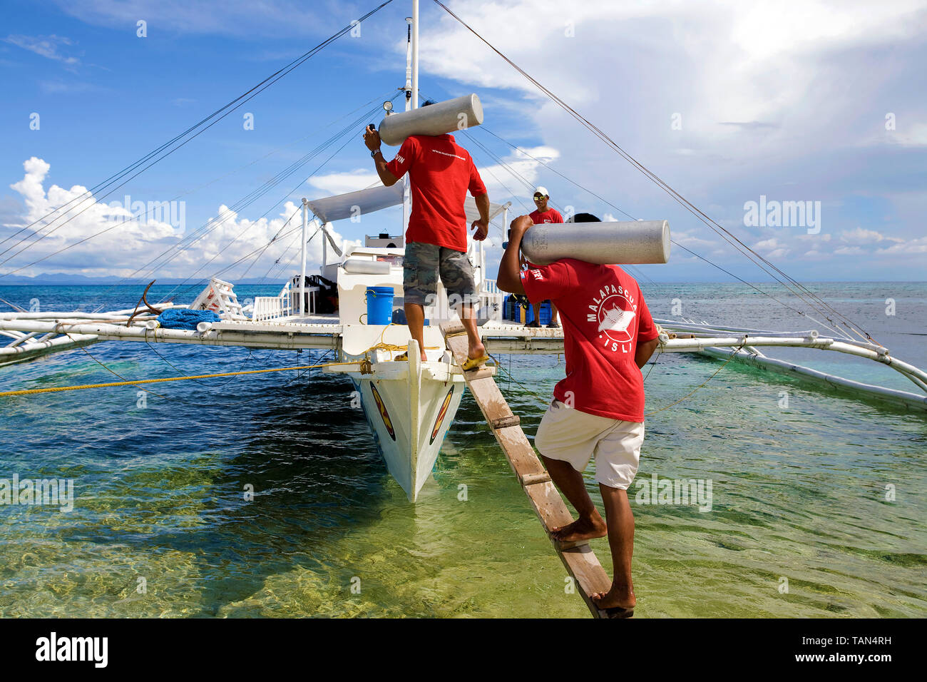 Diving school staff carrying diving cylinders on the diving boat, Bounty beach, Malapascua island, Cebu, Philippines Stock Photo