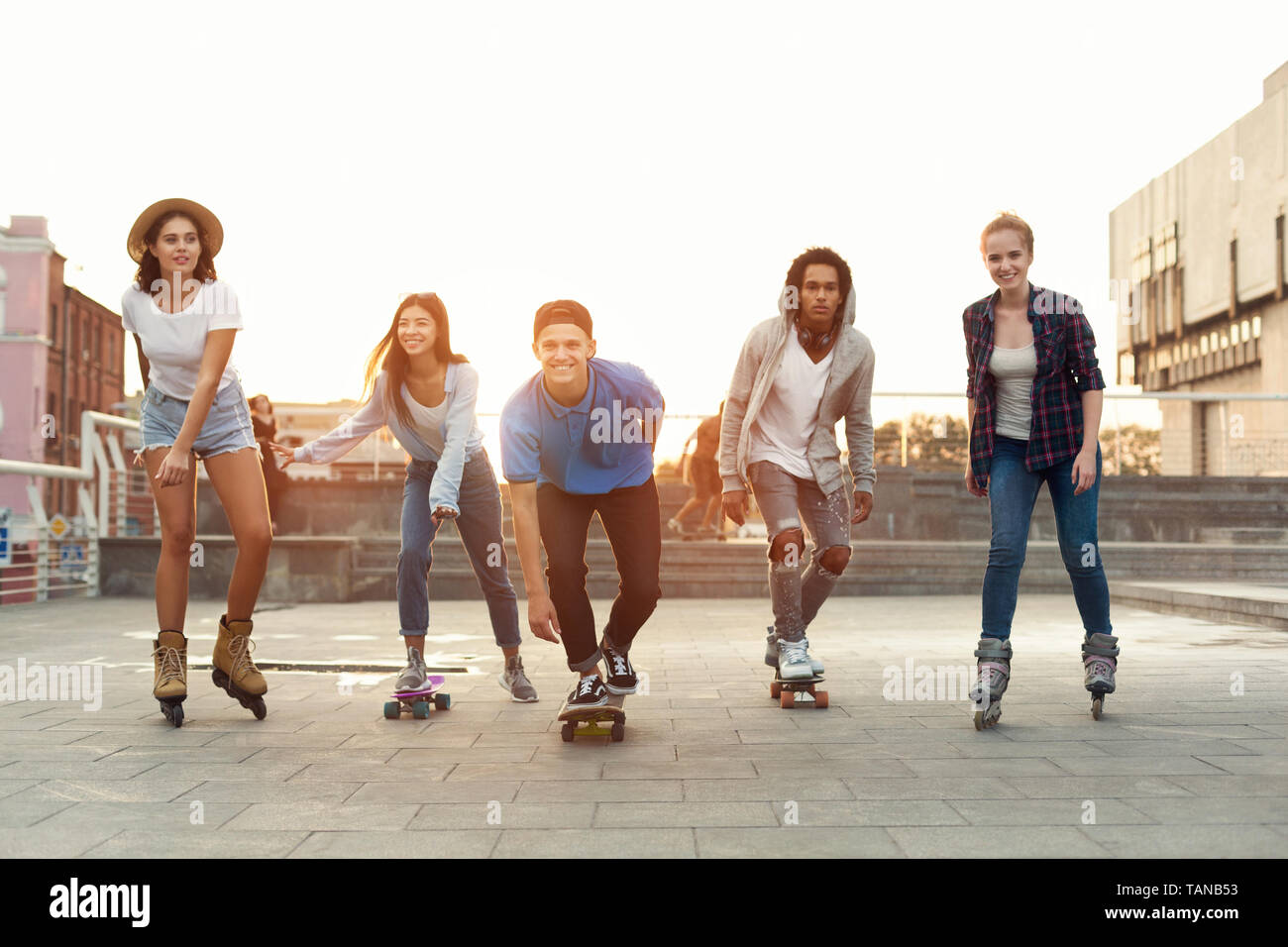 Group of diverse young people skateboarding and rolling in urban area Stock Photo