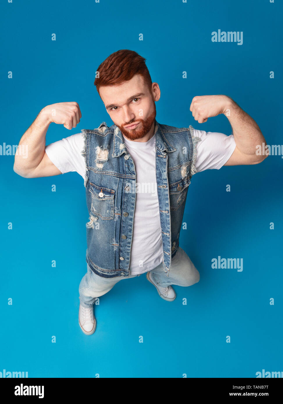 Awesome strong caucasian guy showing biceps on blue background Stock Photo