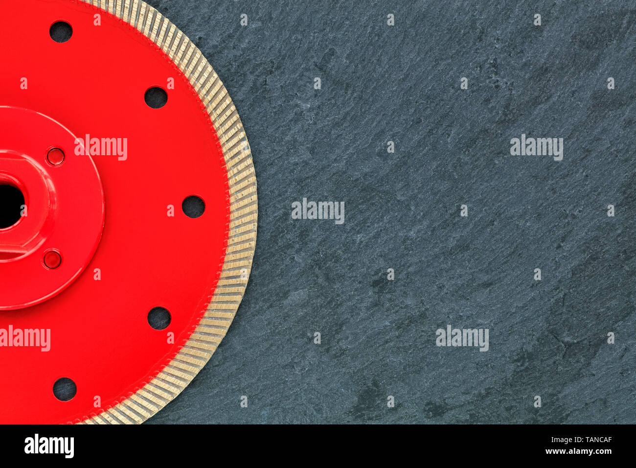 Half of the diamond cutting wheel is red with a threaded nut, on the right side is a copy space on a gray granite background close-up. Stock Photo