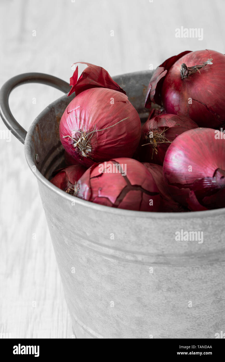 Red onions in a metal pot container with handle. Grey wood background