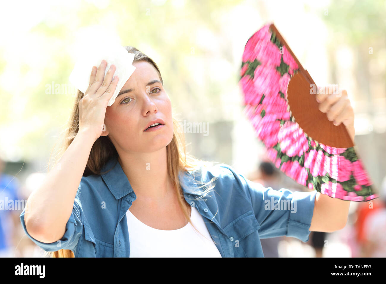 Sad woman fanning and sweating suffering a heat stroke on summer in the street Stock Photo
