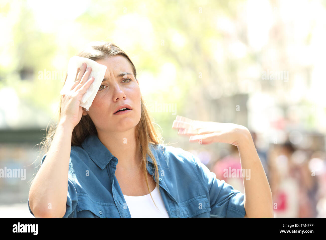 Unhappy woman sweating suffering a heat stroke and fanning with the hand in the street on summer Stock Photo